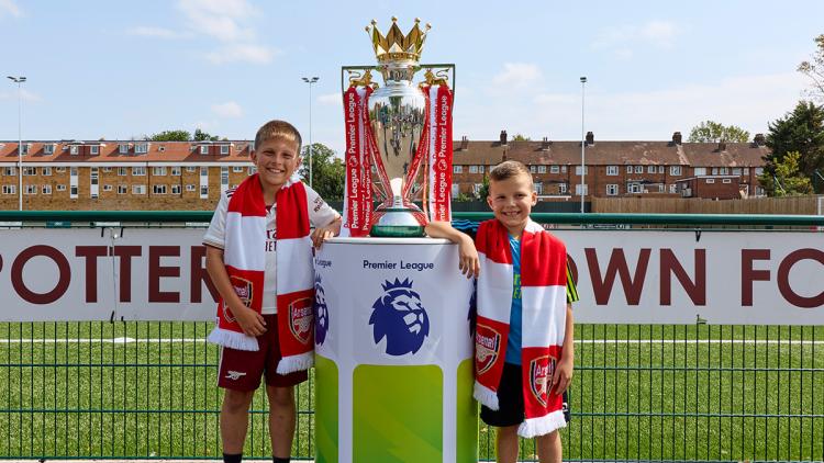 Children wearing Arsenal scarves stand with the Premier League Trophy